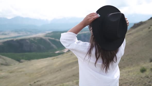 Attractive Brunette in a Hat and White Shirt Is Enjoying Nature in the Mountains. Beautiful Young