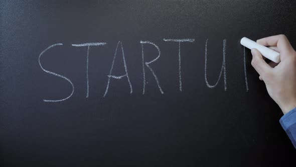 Startup written on chalkboard. Hand writing word Startup with white chalk on blackboard