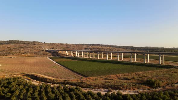 Aerial view of a long road bridge over a landscape with fields and meadows at sunset in Israel