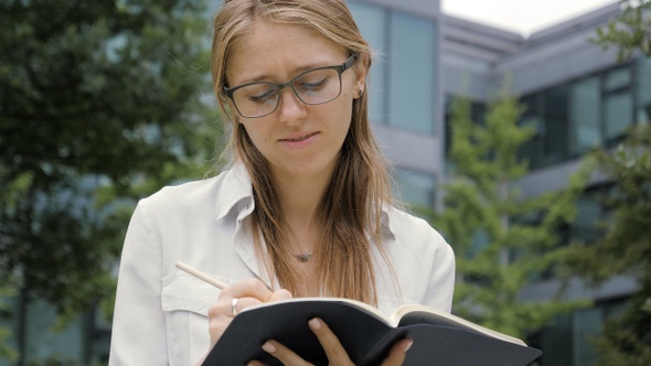 Beautiful Pensive Young Student in Glasses Is Holding A