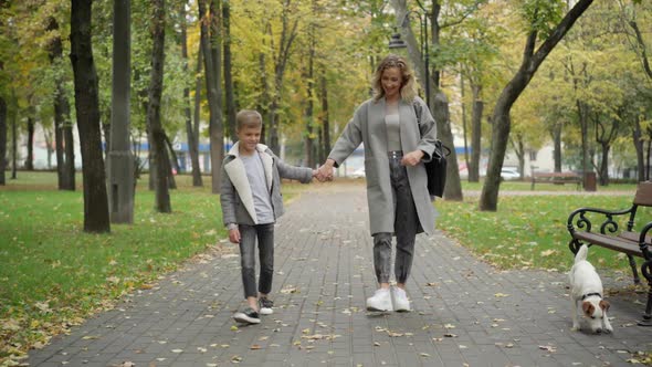 Wide Shot Portrait of Happy Caucasian Mother and Son Walking Along Park Alley on Autumn Day Outdoors