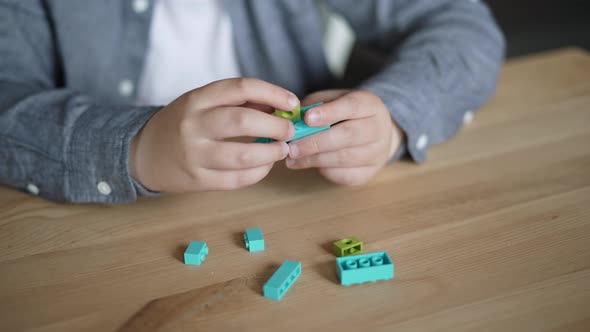 Caucasian Child Collects Toy Man From Plastic Constructor on Table Closeup