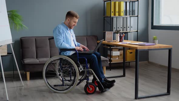Disabled Person Freelancer is Working with Laptop Typing Sitting in Wheelchair at Office