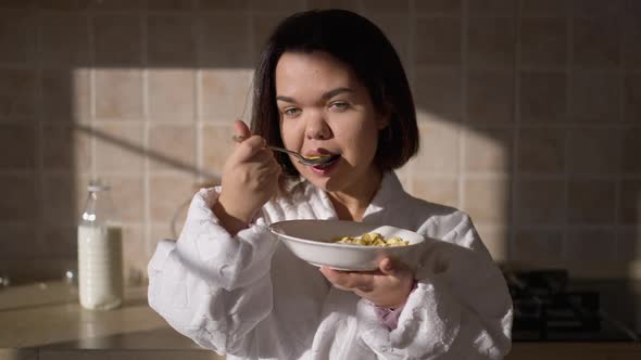 Portrait of Smiling Charming Little Woman Eating Morning Cereals with Milk Standing in Kitchen at