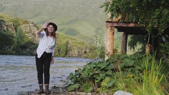 Attractive Brunette in a Hat and a White Shirt in Peas Enjoys Nature in the Mountains. Young Woman