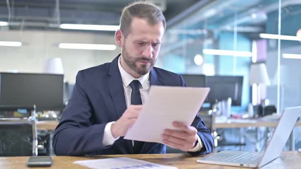 Upset Young Businessman Reading the Documents in Office