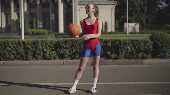 Wide Shot Portrait of Confident Smiling Caucasian Woman in Retro Sportswear Bouncing Basketball Ball