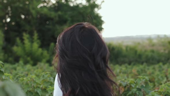 Seductive Brunette Corrects Long Hair Among Green Plantation and Gazing