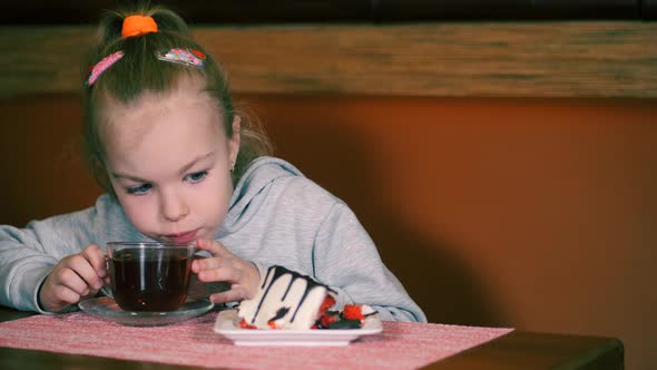 Little Girl Eats Dessert with Fresh Strawberries and Drinks Tea