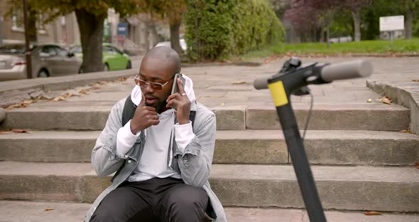 Black Man Sitting on the Stairs Near an Electric Scooter