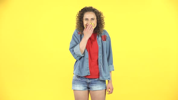 Girl Playing Flirts, Laughs and Looks Around with Red Lips in Kiss on Yellow Background at Studio