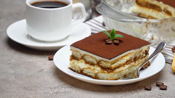 Traditional Italian Tiramisu dessert in glass baking dish and portion on grey concrete background