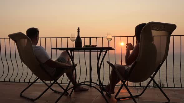 Beautiful Young Couple Drinking Wine on the Terrace and Admiring the Sunset Over the Sea