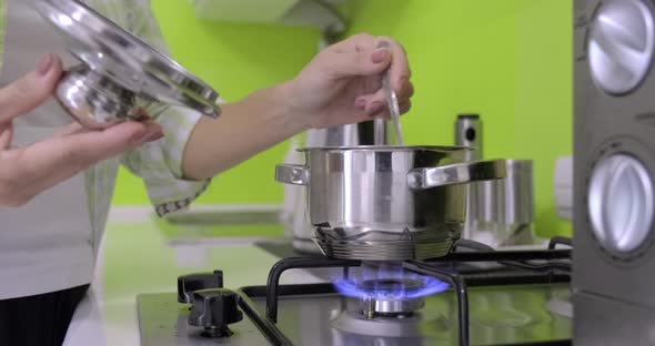 Woman Cooking in a Small Metal Pan on Gas Burner in Kitchen