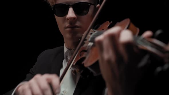 Young Caucasian Male in Black Suit and Glasses Plays Violin on Dark Background