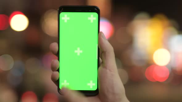 Closeup of Young Man Using Phone with Green Screen Against Illuminated Lights at Night