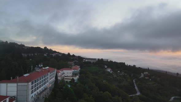 Aerial forward over Golden Tulip Caramulo hotel and surrounding landscape at sunrise on cloudy day,