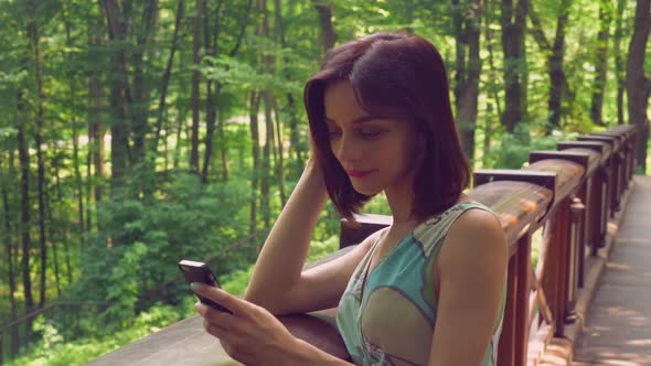 Brunette Female Rests on a Wooden Railing at the Elbows and a Message on the Cell