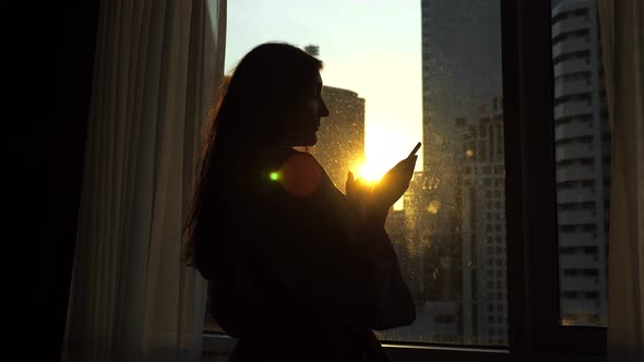 Girl in Bathrobe Uses Phone Standing Near Window in Hotel