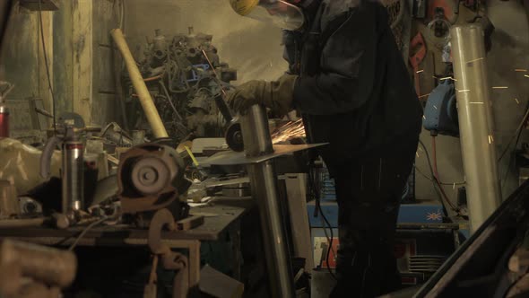 Man in messy workshop angle grinding steel plate on stainless steel piping