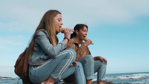 Side view of a Caucasian and a mixed race girl eating ice cream seaside