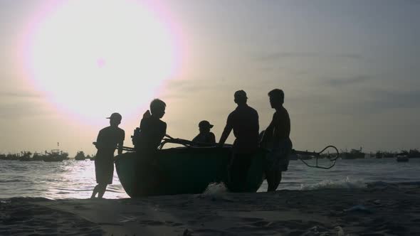 Fishermen Silhouettes Haul Round Boat To Beach at Backlight