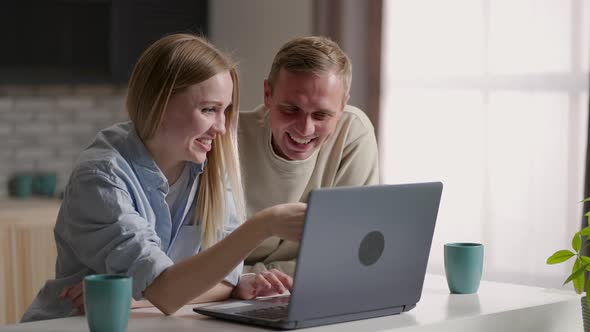 Bonding Millennial Smiling Couple Looking at Laptop Screen Choosing Goods in Online Store Involved