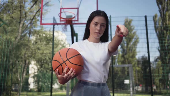 Attractive Brunette Woman with a Basketball Ball Challenging Viewer Pointing Her Finger