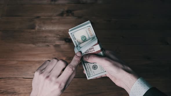 Male Hands Hold Three Stacks of 10000 US Dollar Bills on Wooden Background