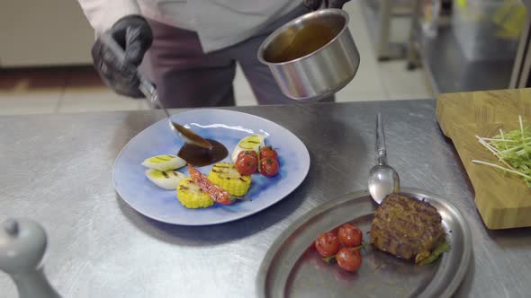 The Chef Pouring Sauce on the Plate with Grilling Meat, Corn, Cherry Tomatoes, Lemongrass and Chili