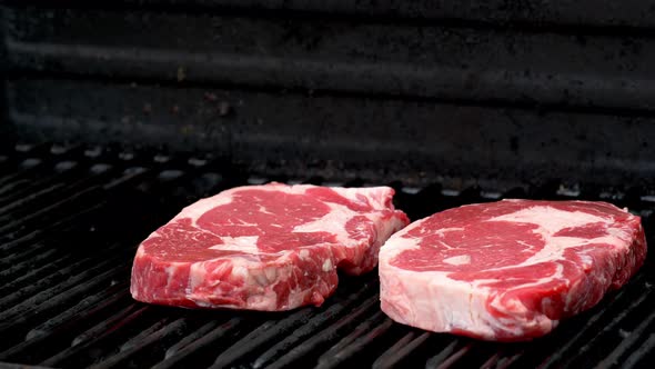 Two raw rib-eye steaks getting ready to cook on a grill.