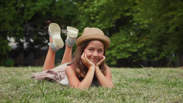 A cute smiling girl in a straw hat lies on the lawn and looks around. Slow motion