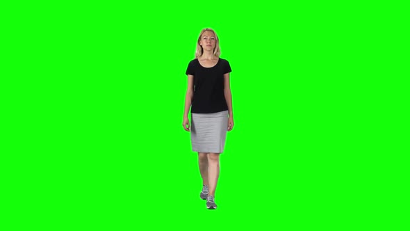 Blonde Girl in a Black T-shirt, Grey Skirt and Sneakers Going Against a Green Screen. Slow Motion