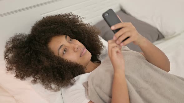 Smartphone Use By Young African Woman Laying in Bed