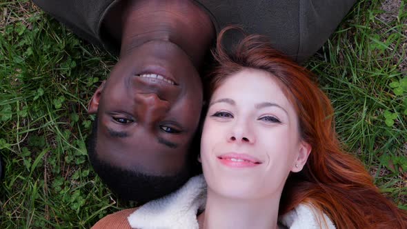 Portrait Of young attractive  Mixed Race Couple lying on the grass smiling at camera