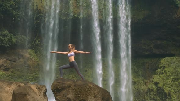 Young Woman Does Yoga on Rock Against Waterfall