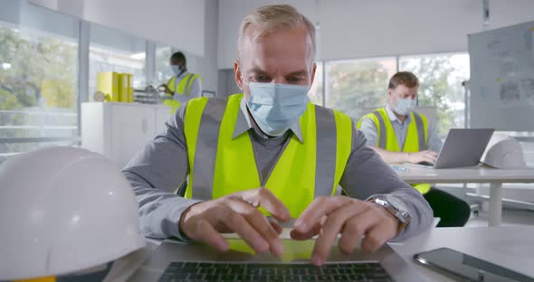 Mature Architect in Face Mask Working on Laptop Sitting at Table in Office