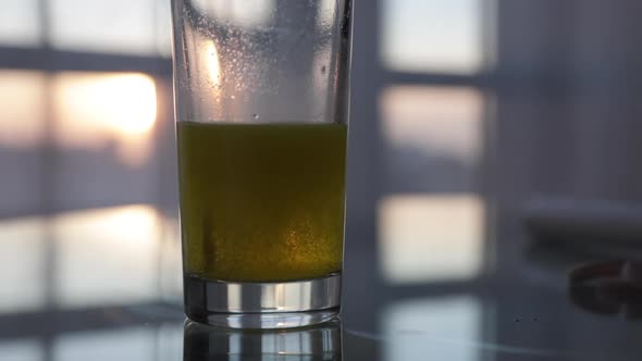 Effervescent yellow tablet dissolves in glass of water, golden sunset background