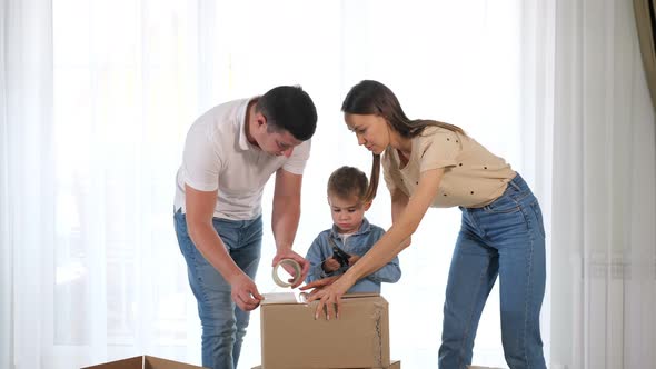 Young Couple Helps Small Son Pack Large Box with Duct Tape