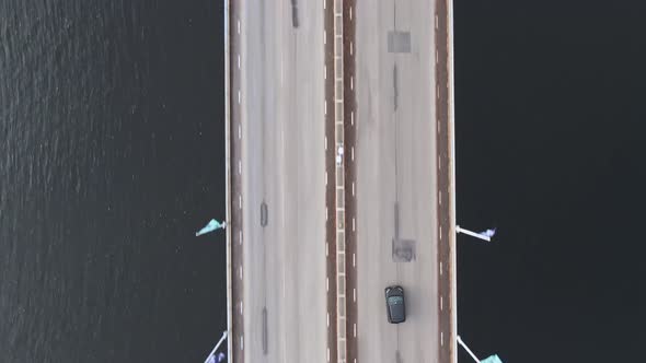 Vehicle driving through highway bridge over water in aerial top-down view
