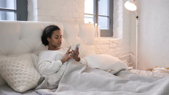 Young African Girl Celebrating Success While Using Smartphone in Bed