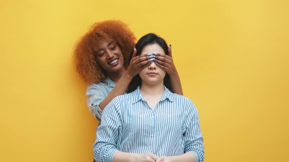 Young African American Black Woman Releasing Hands From Her Asian Firends Eyes and Surprising Her