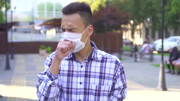 Young Asian Man with a Medical Mask on the Face Coughing and He Uses a Smartphone Slow Mo