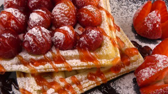 Belgian waffles with strawberry, sweet strawberry topping and powdered sugar on a stone board.