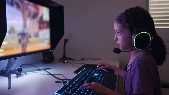 Young girl sitting in front of a computer, playing a game wearing a headset