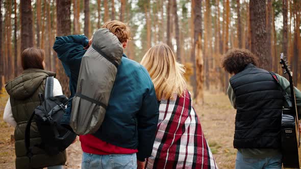 Unknown Young Friends with Backpack Guitar and Packed Tent are Walking By Path in Autumn Wood