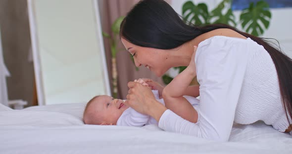 Portrait a Beautiful Young Mother Kisses the Baby and Holds His Hands