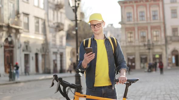 Portrait of a Happy Delivery Man Who is Standing and Texting on a Smartphone