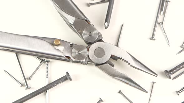 Metal Round-nose Pliers Among Nails on White, Rotation, Close Up