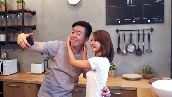 sian couple using smartphone for selfie while cooking in the kitchen at home.
